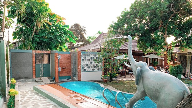 Una piscina con un sendero de piedra que la conduce, rodeada de vegetación y un edificio con techo de tejas.