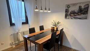 Et spiseområde med et træbord og stole, hængende lamper, en radiator og et vindue med gardiner.