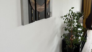En moderne stue med minimalistisk indretning, med et stort abstrakt kunstværk på væggen, en potteplante og et slankt, sort TV-møbel.