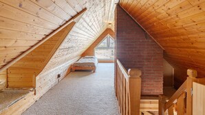 Un dormitorio de madera en el ático con techo inclinado, pared de ladrillo y escalera de madera.