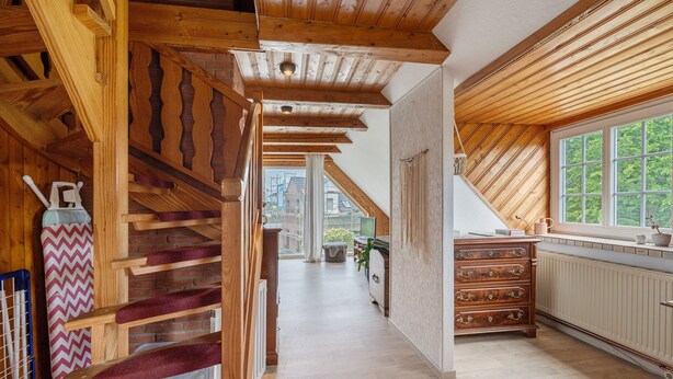 Una escalera de madera que lleva a un dormitorio tipo loft con vistas al exterior.