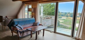 A room with a sofa, a table, and a view of a landscape through large windows.