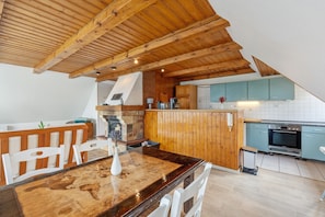 A kitchen with wooden ceiling beams, a dining table with chairs, a brick wall, and a tiled backsplash.