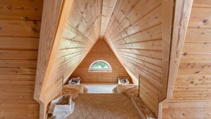 Un dormitorio de madera en el ático, con techo inclinado, una ventana pequeña y una cama acogedora.