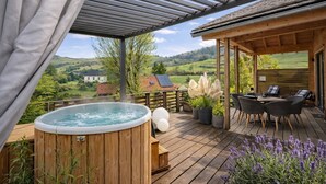 A wooden deck with a hot tub, outdoor seating, and a view of a green landscape.