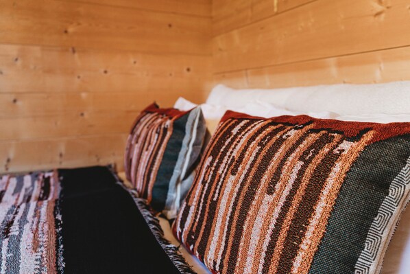 Interior de una cabaña de madera con una cama con ropa de cama a rayas y almohadas.