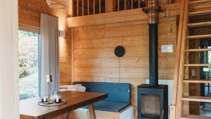 A wooden interior with a bench, a table with glasses, a stove, and a window with curtains.