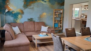 A living room with a brown sofa, a coffee table, a bookshelf, and a dining area with chairs. - Apartment 'Ferienwohnung Ebbe' with Shared Garden, Balcony and Wi-Fi (Pellworm)