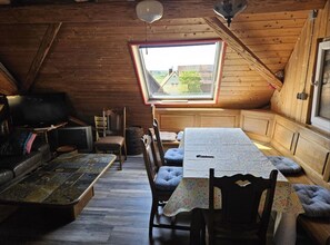 A cozy attic room with a sloped ceiling, a small window, a wooden table, and a sofa. - Rustic Country House with Private Terrace, Shared Garden, and Wi-Fi (Colmberg)