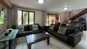 A living room with a sofa set, a coffee table, and a dining table with chairs. There is a staircase leading to an upper level. - San Lameer Villa 2802 (Southbroom)