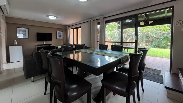 A dining area with a large table, chairs, a television, and a refrigerator. - San Lameer Villa 2802 (Southbroom)