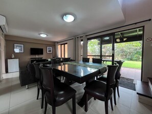 A dining area with a large table, chairs, a television, and a refrigerator. - San Lameer Villa 2802 (Southbroom)
