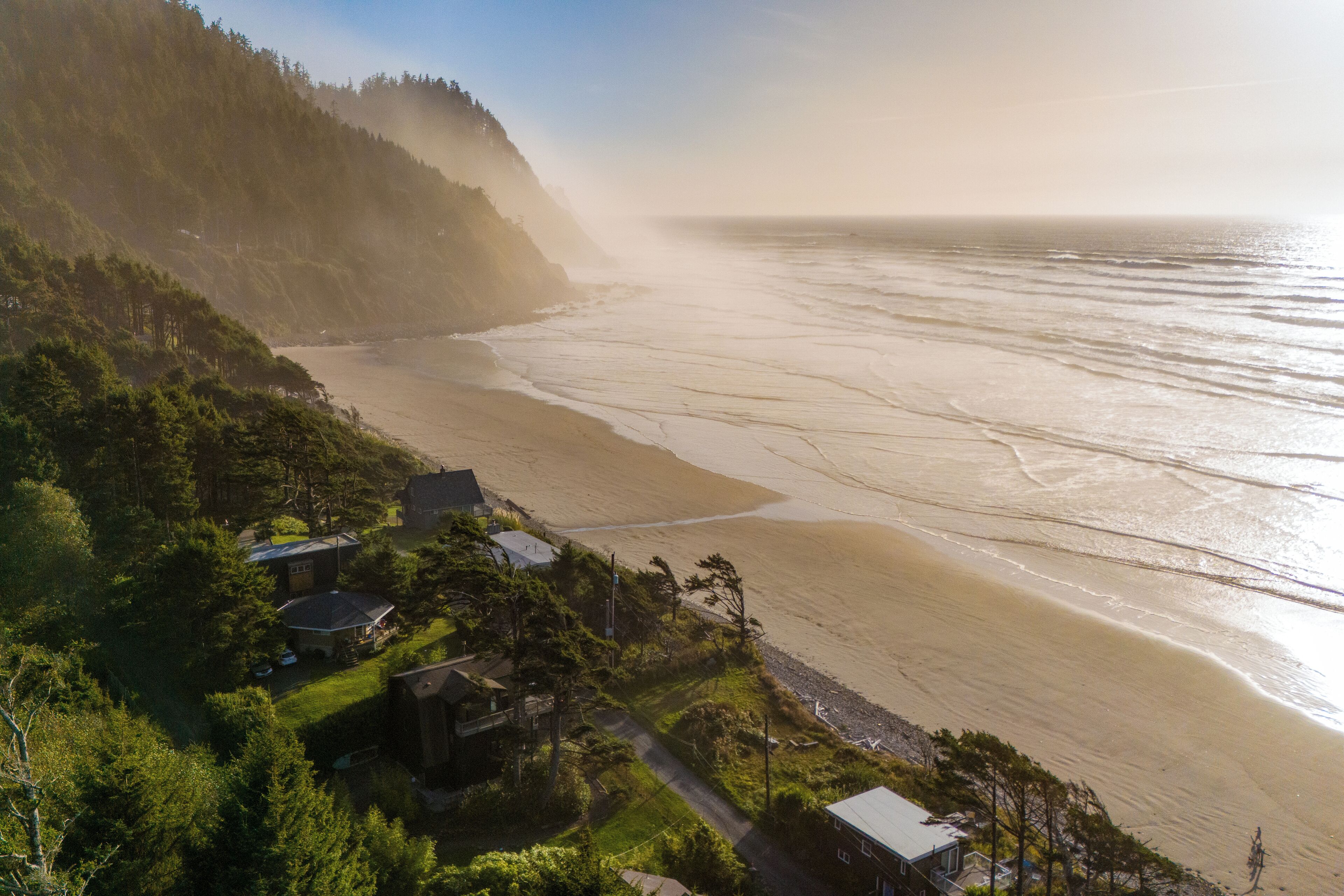 A coastal landscape with a beach, houses, and forested hills.