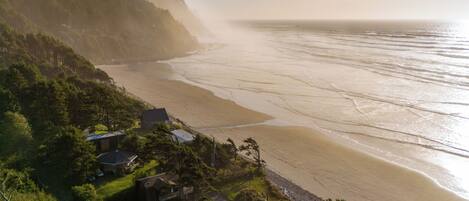 A coastal landscape with a beach, houses, and forested hills.