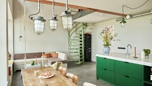 A modern kitchen with green cabinets, a wooden dining table, and hanging pendant lights.