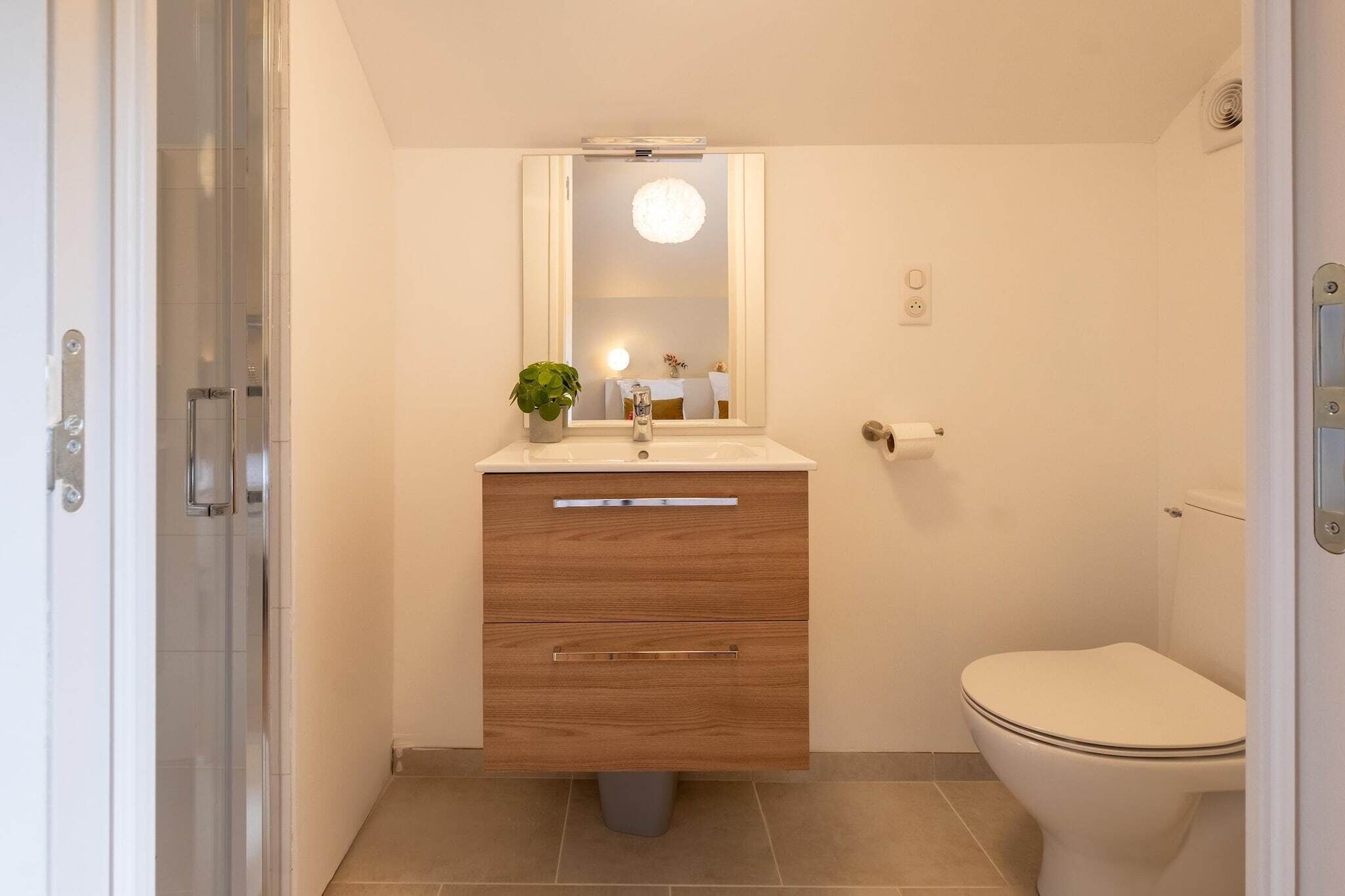 A modern bathroom with a wooden vanity, a toilet, and a glass shower enclosure.