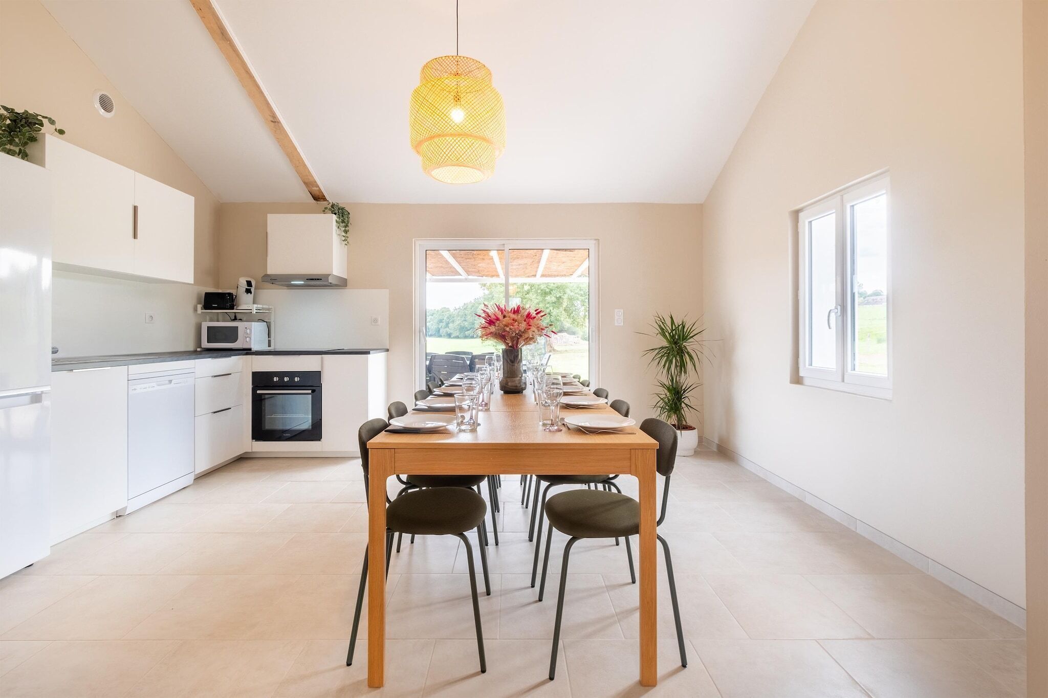 Une cuisine moderne avec des meubles blancs, une table à manger pour quatre personnes et un luminaire suspendu.