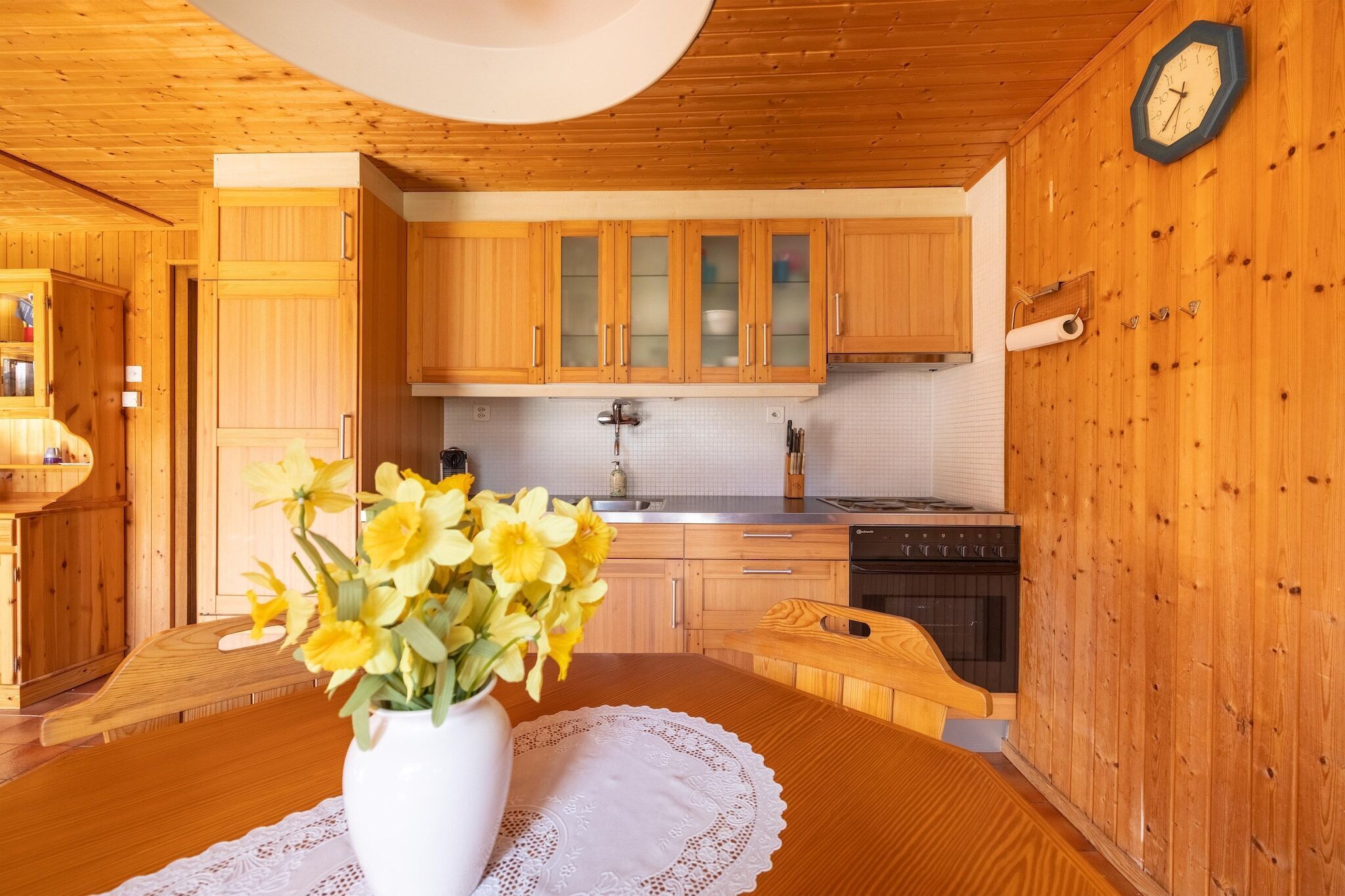 Une cuisine en bois, avec des placards, un fourneau et une horloge au mur.