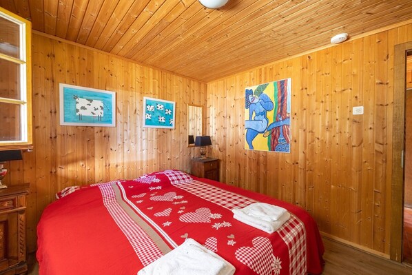A wooden-paneled room with a bed, a nightstand, and a painting on the wall.