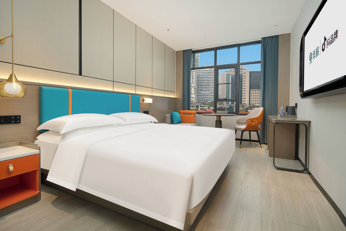 A modern hotel room with a large bed, a desk, and a view of the city.