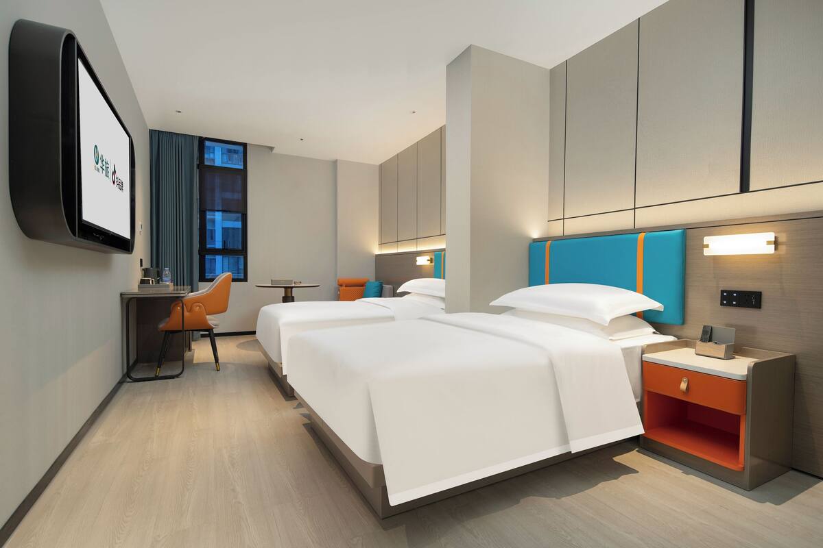 A modern hotel room with two beds, a desk, and a TV.