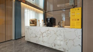 Una moderna zona de recepción de hotel con mostrador de mármol, una máquina de café y un separador de vidrio.