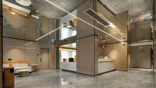 Un moderno vestíbulo de hotel con mostrador de recepción, zona de estar y una cocina visible a través de una división de vidrio.