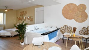 Een moderne hotelkamer met een ruime badkuip, een zithoek met een tafel en stoelen, en een kamerplant.
