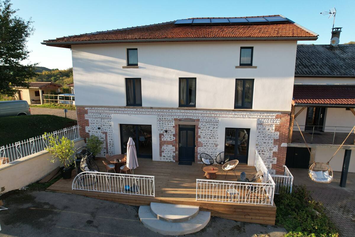 Une maison à deux étages dotée d’une terrasse en bois, d’un espace salon extérieur et d’un fauteuil suspendu.