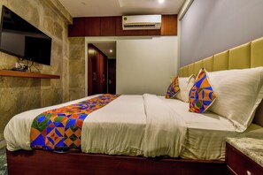 A hotel room with a bed, a television mounted on the wall, and an air conditioning unit.
