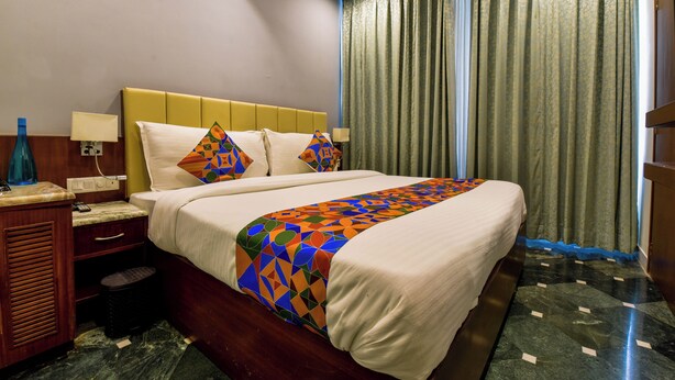 A hotel room with a bed, nightstand, lamp, and curtains.