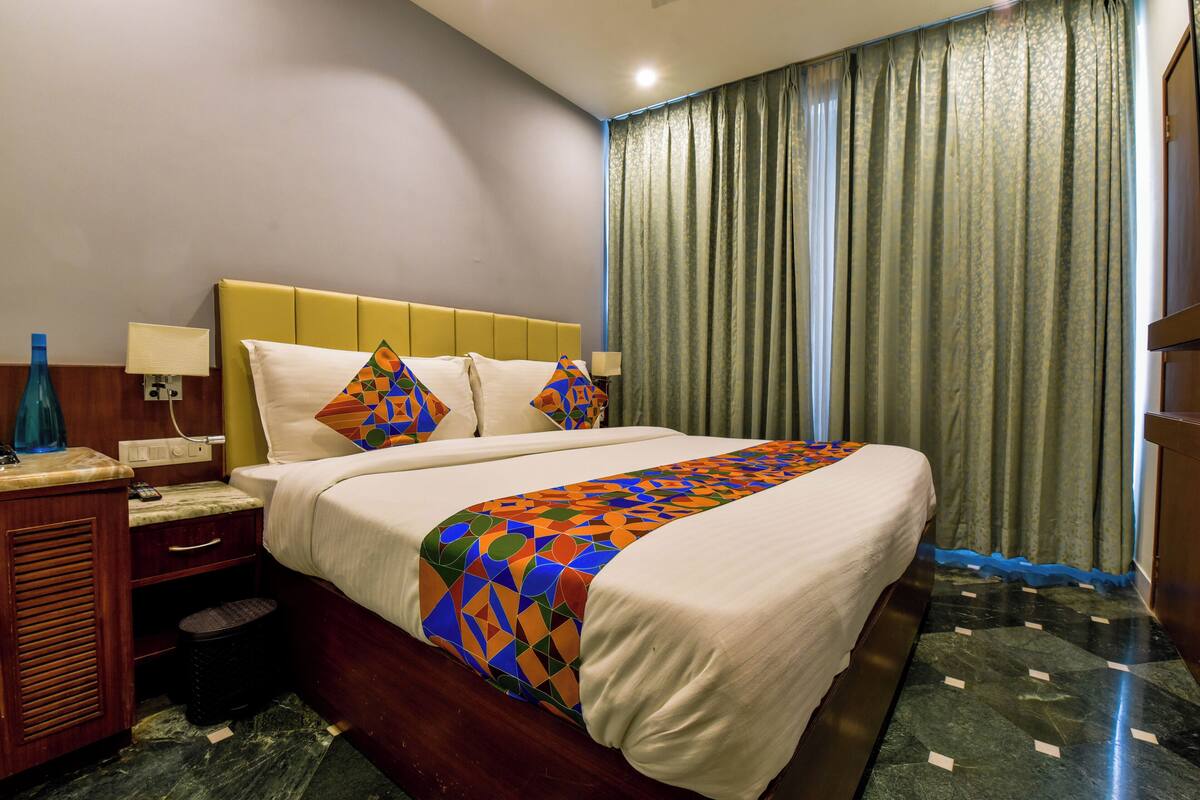 Une chambre d’hôtel avec un lit, une table de chevet, une lampe et des rideaux.