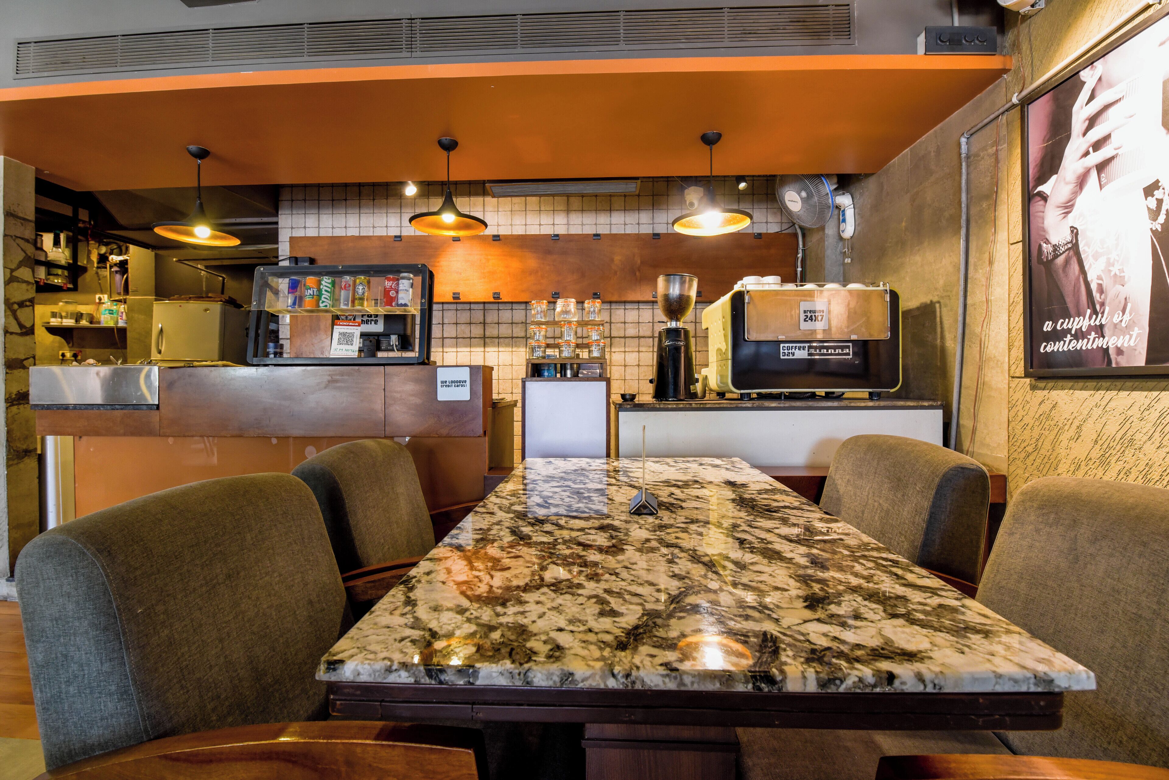 A restaurant with a marble-top table, cushioned chairs, pendant lighting, a coffee machine, and a menu board.
