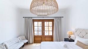 Una habitación de hotel con una cama grande, un sofá, una mesita de noche con lámpara y un ventanal con cortinas.