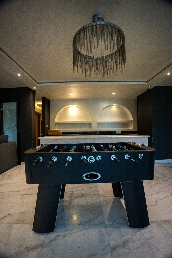 A foosball table in a modern room with a chandelier and recessed lighting.
