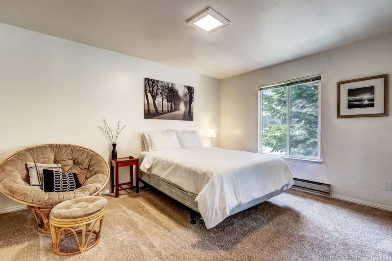 A bedroom with a bed, a chair, a nightstand, a window, and a painting on the wall.