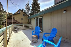 A covered outdoor area with a table and chairs, a small stool, and a sliding glass door leading to an interior space.