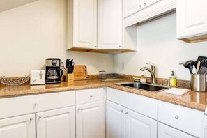 A kitchen with white cabinets, a coffee maker, a toaster, a sink, and a knife block.