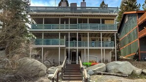 Un immeuble à plusieurs étages, avec un escalier menant à une porte, entouré de rochers et d’arbres.