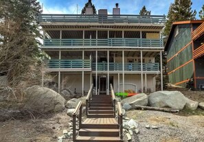 A multi-story building with a staircase leading to a door, surrounded by rocks and trees.
