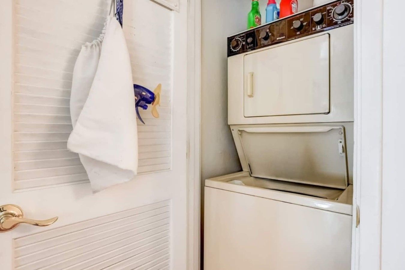 A laundry room with a white washing machine and dryer, a towel hanging on the door, and a window with blinds.