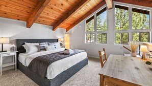 Een slaapkamer met een groot bed, een houten plafond en uitzicht op bomen door grote ramen.