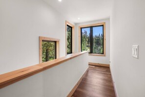 A hallway with wooden beams, white walls, and two windows with wooden frames.