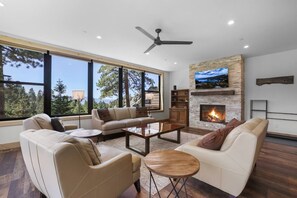 A modern living room with a fireplace, large windows, and a ceiling fan.