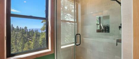 Ducha con paredes de vidrio y vistas a un bosque a través de una ventana.