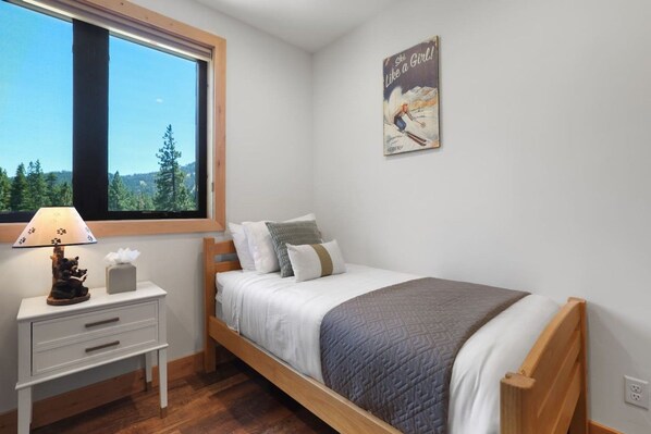 A bedroom with a bed, a nightstand, a lamp, a window with a view, and a poster on the wall.