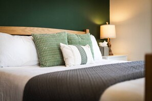Un lit bien fait, avec une tête de lit en bois, des oreillers blancs et verts, et une couverture grise.