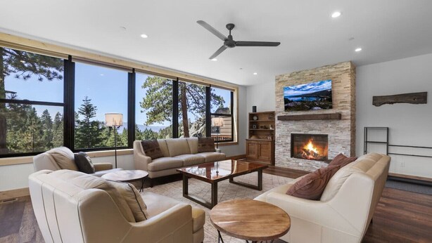 A modern living room with a fireplace, large windows, and a ceiling fan.
