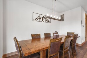 Une salle à manger avec une table et des chaises en bois, un lustre et des œuvres d’art accrochées au mur.