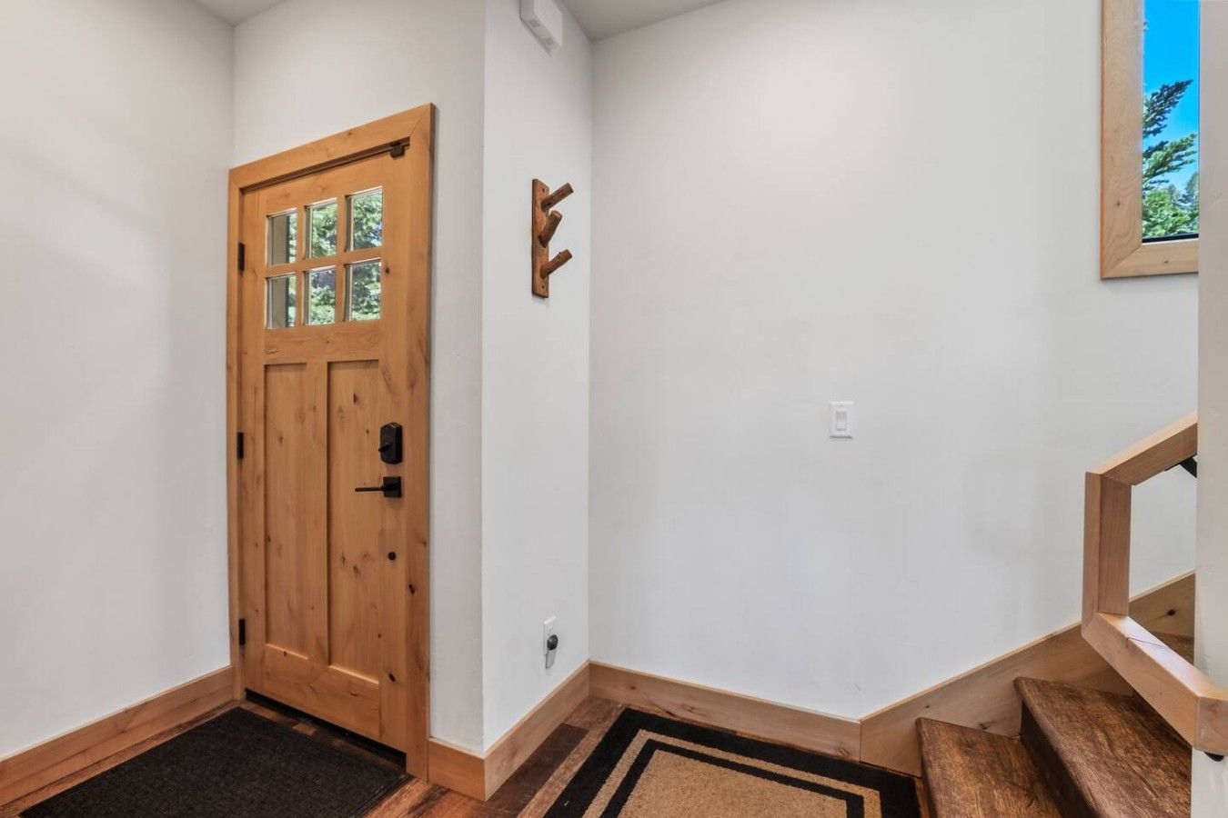 A hallway with a wooden door, a coat rack, and a small window with a view of trees.